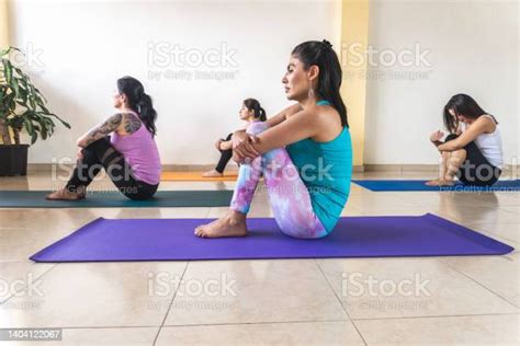 Women In A Yoga Class Sitting On The Mat Hugging Their Knees Stock