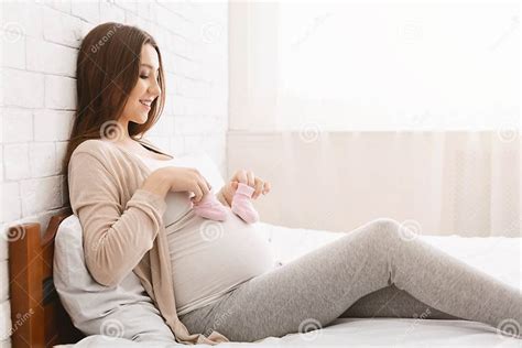 Pregnant Woman Playing With Tiny Shoes Stepping On Belly Stock Photo