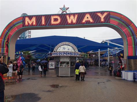 People Are Walking Under The Midway Sign At An Amusement Park