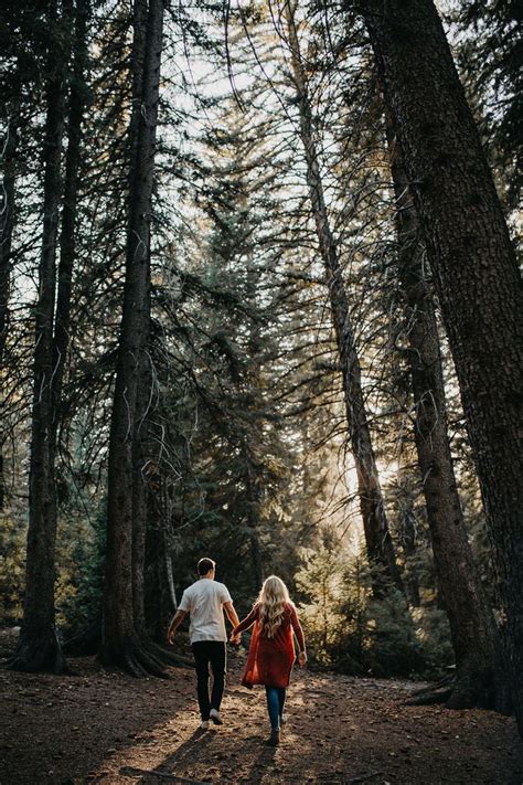 A Couple Walking Through The Woods Holding Hands