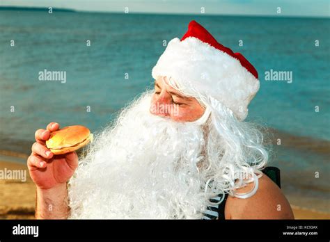 Santa Claus On The Beach Eating A Hamburger The Concept Of Unhealthy