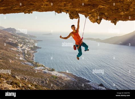Male Rock Climber Hanging On Cliff With One Hand And Showing Thumb Up