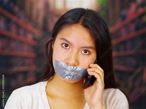 Young Brunette Woman Wearing White Sweater Gagged With Duct Tape Covering Mouth Facing Camera