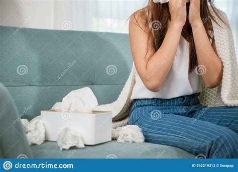 Sick Female Sitting Under Blanket On Sofa And Sneeze With Tissue Paper