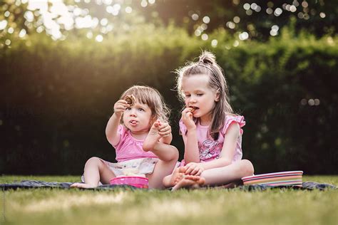 Two Cute Girls Outdoors Sitting On The Grass Having A Snack By