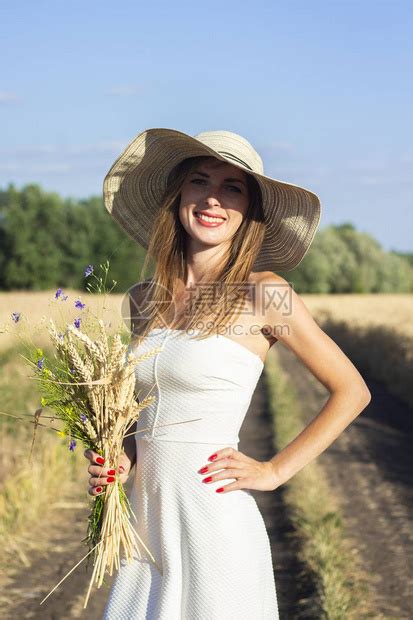 穿着白色礼服和帽子的年轻美女在牛奶田之间的公路上拿着一束带野花的束户外娱乐概念高清图片下载 正版图片 摄图网