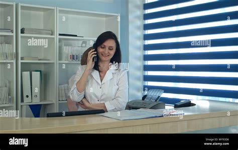Smiling Female Nurse Answering Phone Call At The Reception Desk Stock