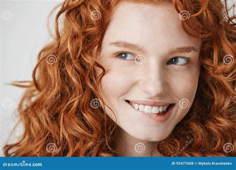Close Up Of Beautiful Girl With Curly Red Hair And Freckles Smiling Biting Lip Over White