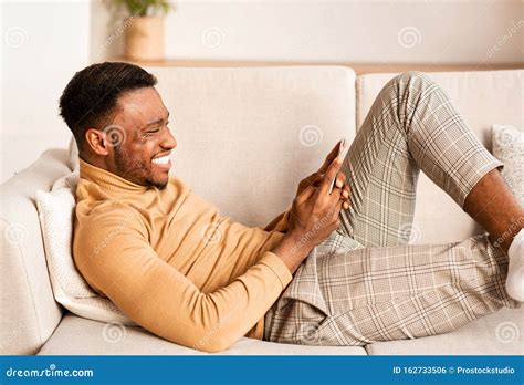 Relaxed Guy Using Smartphone Lying On Sofa At Home Stock Photo Image