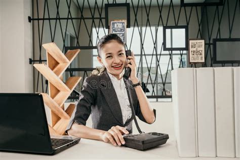 Young Female Employees Sitting At Office Desks And Talking On The Phone