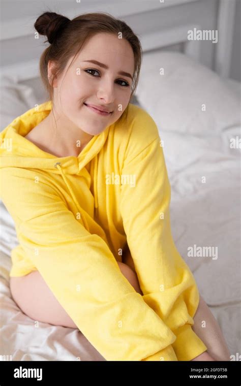 Happy Cheerful Brunette Girl In Yellow Hoodie In White Bedroom Sitting