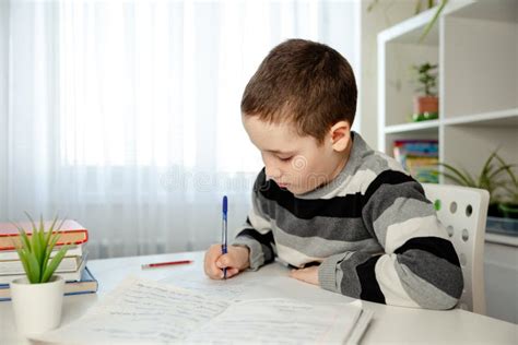 Kid Learning While Sitting On Desk At Home Pupil Writing In Notebook