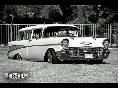 black and white photo of an old car parked in the grass next to a fence