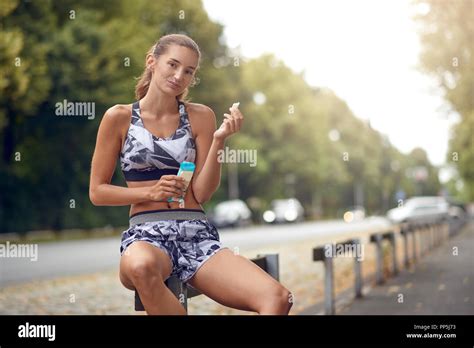 Sporty Attractive Slender Young Woman Sitting On A Roadside Rail Eating