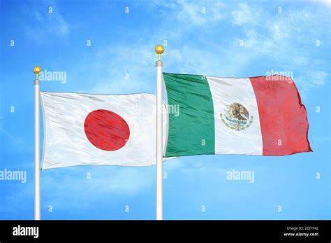 Japan And Mexico Two Flags On Flagpoles And Blue Cloudy Sky Stock Photo