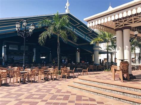 An Outdoor Dining Area With Tables Chairs And Palm Trees In Front Of A