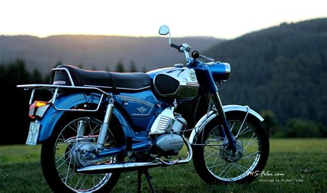 a blue motorcycle parked on top of a lush green field with mountains in