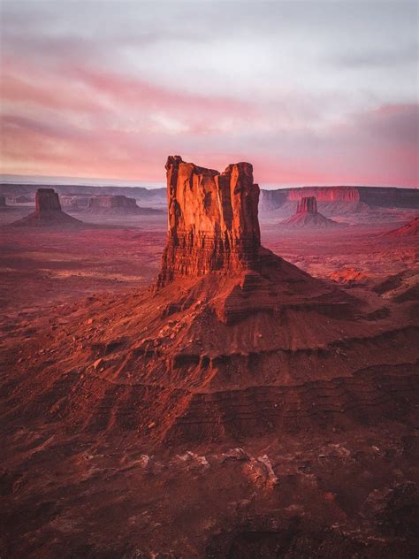 A Large Rock Formation Sitting In The Middle Of A Desert Under A Pink