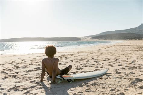 Free Photo Chilling Man Sitting On Beach With Surfboard