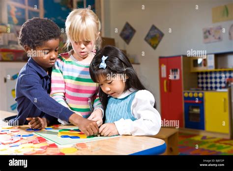 Three Preschool Children Working Together On Colorful Shape Puzzle