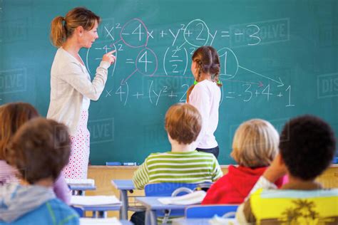 Primary School Teacher Explaining Equation On Classroom Blackboard