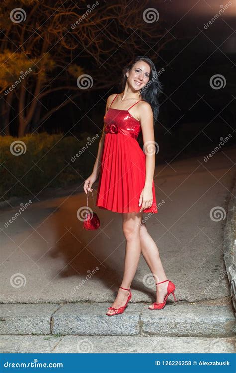 Young Woman In Red Sleeveless Dress Walking In Night Park Stock Photo