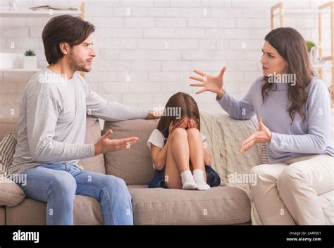 Crying Little Girl Sitting Between Arguing Parents At Home Stock Photo