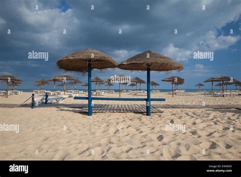 Different Parasols And Sun Loungers On The Empty Beach On Tavira Island