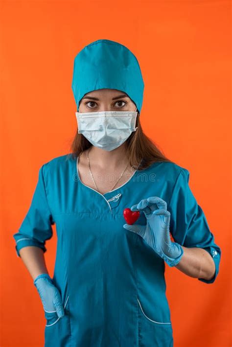 nurse in blue uniform with mask gloves holding small red heart in operating room hospital stock