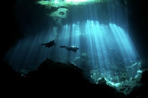 Two People Swimming In An Underwater Cave With Sunlight Streaming Through The Waters Surface