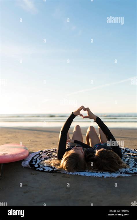 Surfer Girls Lying On The Beach Making Heart Shaped Hands Stock Photo