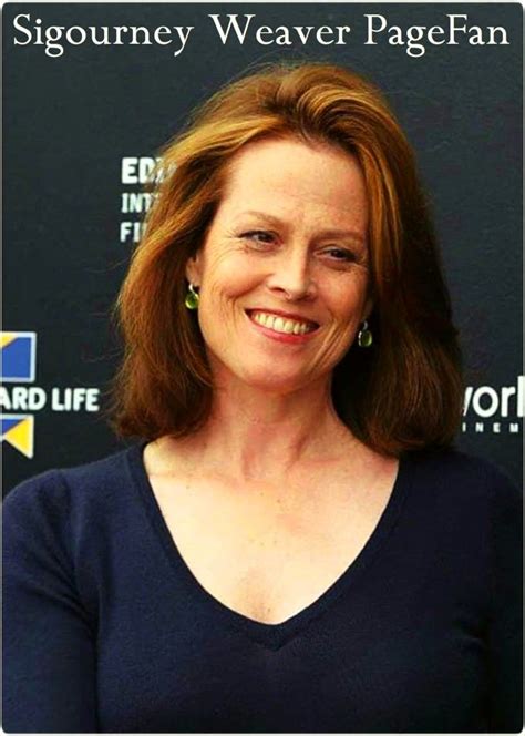 A Woman With Red Hair Smiling At The Camera And Wearing A Blue Shirt Standing In Front Of A