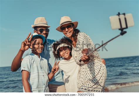 ビーチでスマートフォンを持って自撮りする幸せなアフリカ系アメリカ人の家族の写真素材今すぐ編集