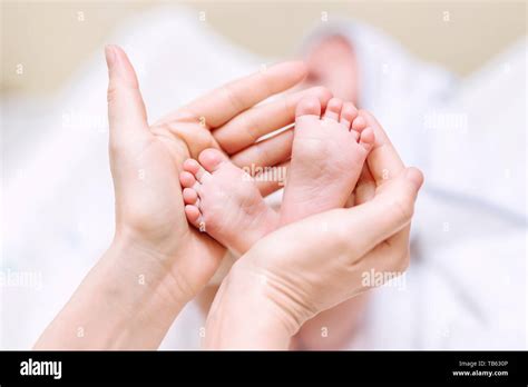 Mother Holding Newborn Baby Feet In Hands Mom Taking Care About Infant