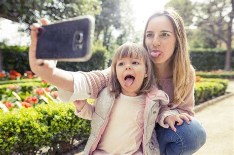 Mother And Babe Sticking Out Tongue While Taking Selfie In Park Stock Photo