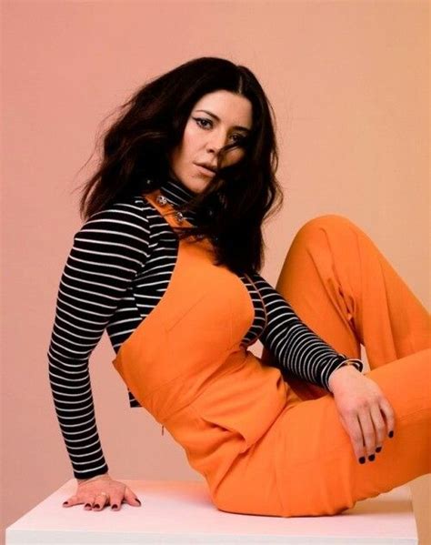 a woman sitting on top of a white table wearing an orange pants and striped shirt