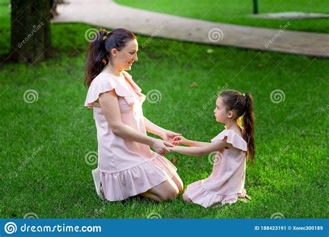 Mother And Daughter 5 6 Years Old Sit In The Park On The Grass And Hold Hands In The Summer A
