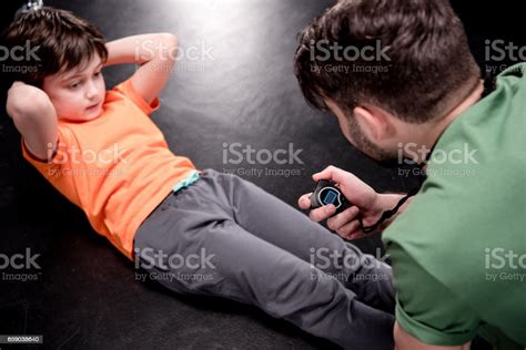 Man Controlling Time While Boy Doing Press Exercise On Black Stock