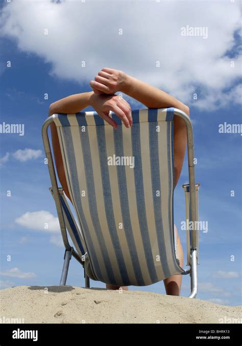 Woman Sunbathing On Deckchair On The Beach Shot Against Blue Sky Stock