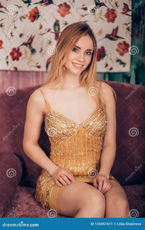 Fashion Portrait Of A Gorgeous Blonde Woman Wearing A Short Shiny Golden Dress And Looking At