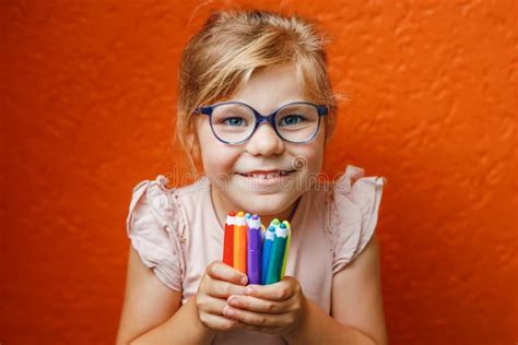 Happy Cute Little Preschooler Girl With Glasses Holding Colorful Pencils And Making Gesture