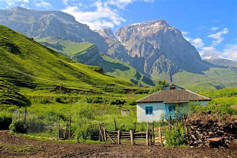 A Small Blue House In The Middle Of A Green Valley With Mountains In