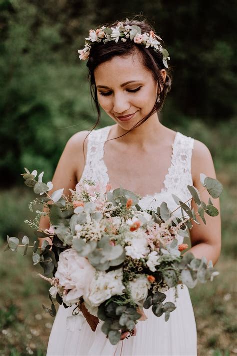 A Woman In A White Dress Holding A Bouquet Of Flowers And Greenery On