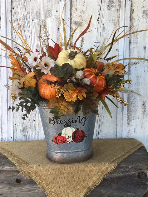 A Bucket Filled With Flowers And Pumpkins On Top Of A Table