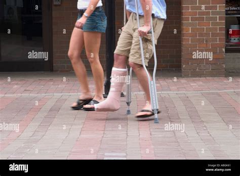 Woman And A Man His Leg In A Cast And Using Crutches Walking On The