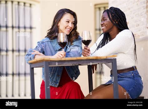 Two Friends Drinking Red Wine Sitting At A Table Outside A Bar