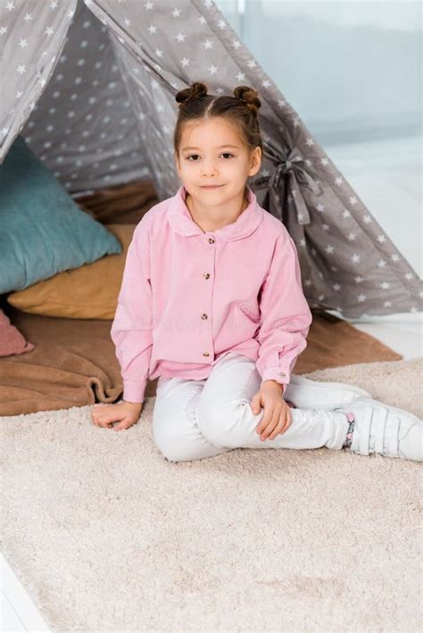 Beautiful Happy Child Sitting On Carpet Near Teepee And Smiling Stock