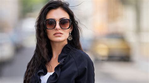 Cute Beautiful Women Model Is Wearing Sunglasses And Black Coat And White Top In Blur Background