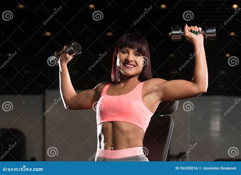 Woman Exercising Shoulders With Dumbbells In The Gym And Flexing Stock
