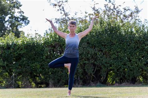 A Middle Aged Woman Practicing Yoga Barefoot Outside In A Grassy Park
